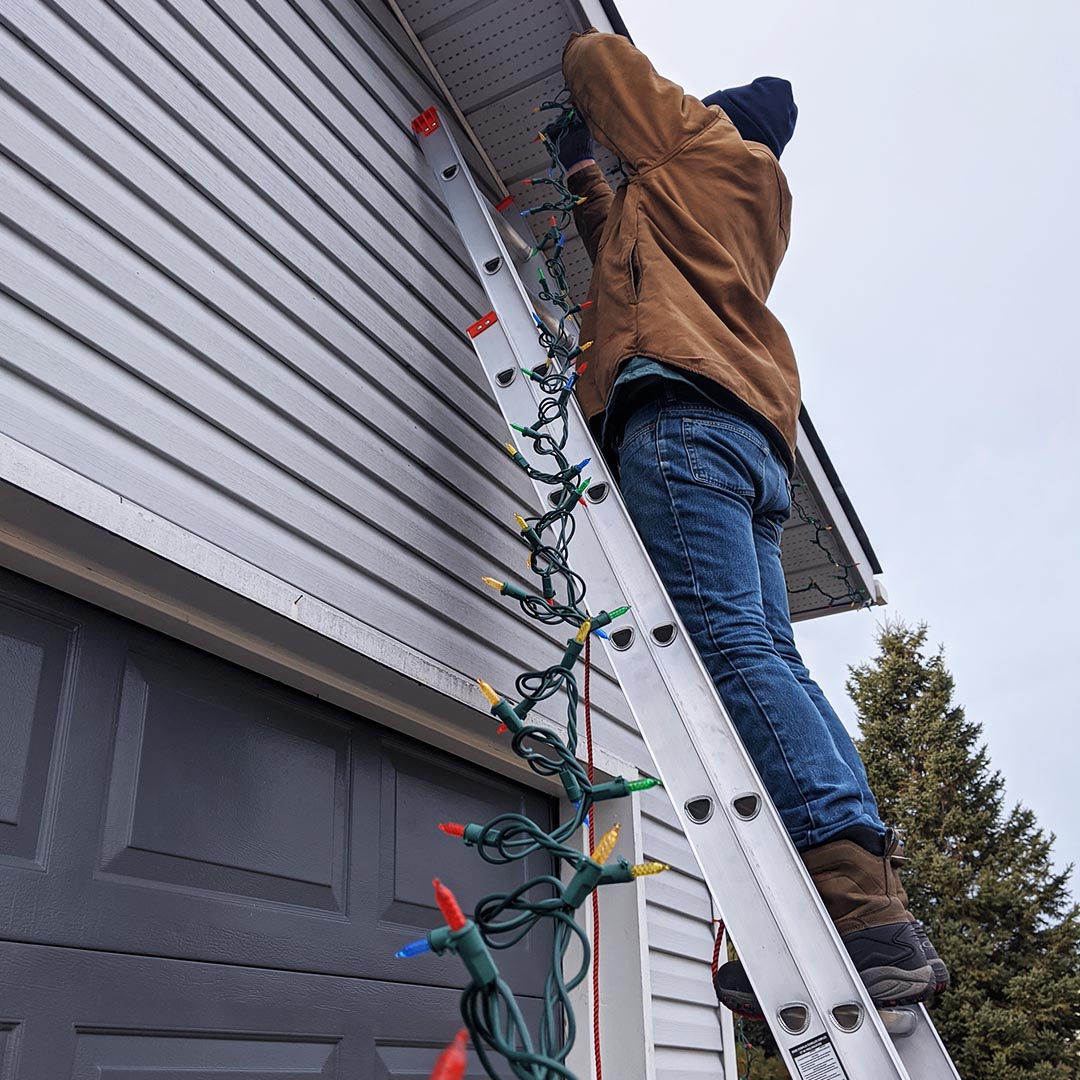 Man on ladder putting up Christmas lights